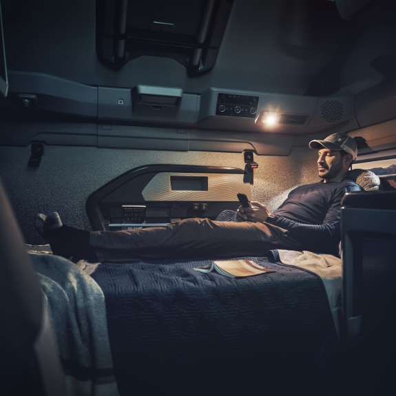 Driver relaxing on a bed in the Volvo VNL truck sleeper cabin