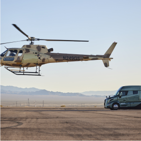 Volvo VNL truck parked on a runway next to a hovering helicopter.
