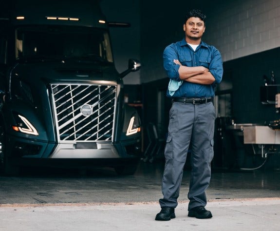 Service technician standing confidently in front of a Volvo VNL truck showing 24/7 Volvo Action Service assistance