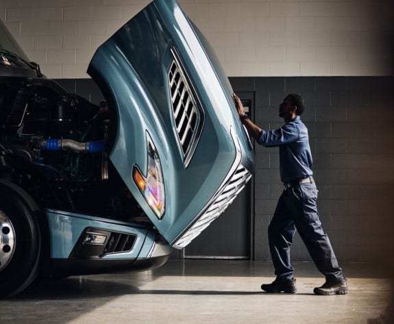 Technician lifting Volvo VNL hood, emphasizing Blue Contract service.