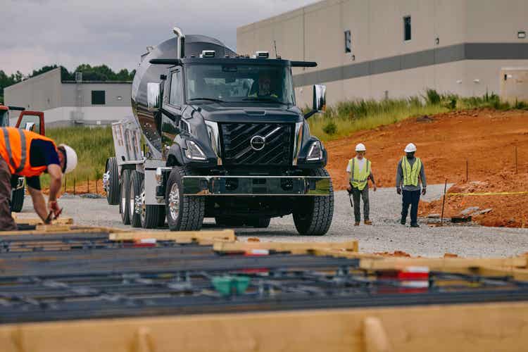 A black colored Volvo VNX truck at a construction site. With cosntruction workers around it.