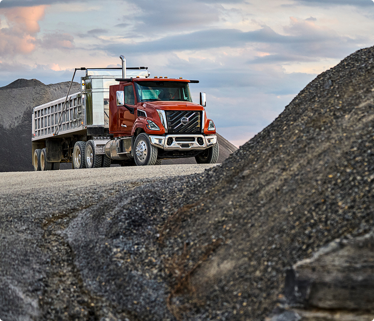 A red color of the Volvo VNX. The truck is on a rocky road. about to climb an uphill road.