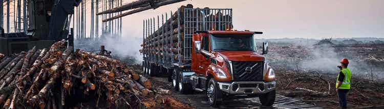 A red Volvo VNX truck that is getting loaded with logs on a site.