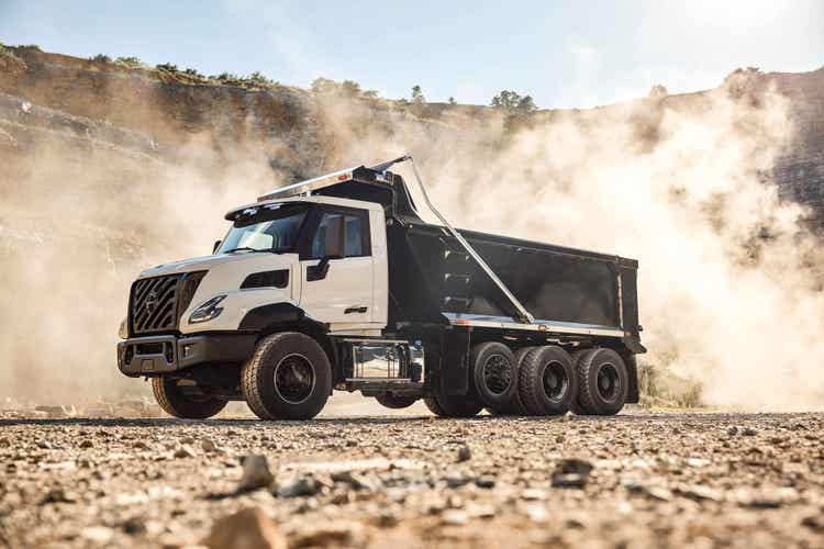 A side view of the Volvo VNX from the ground view of the truck with a dusty, smokey backgorund.
