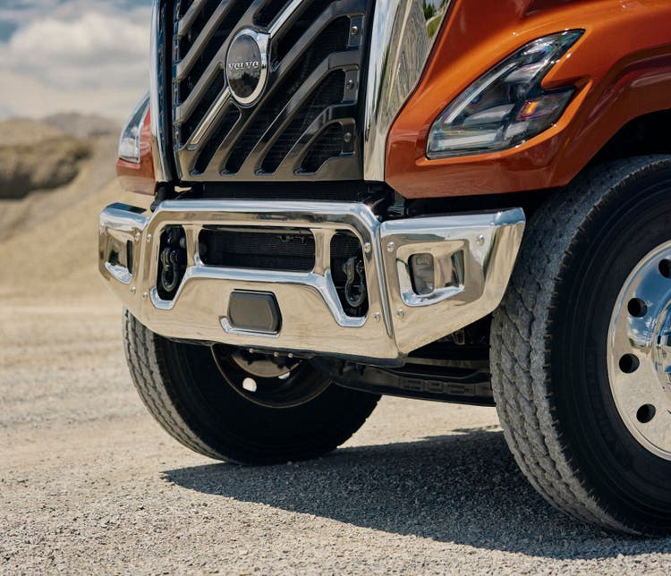 A close-up view of the grille of a reddish orange color Volvo VNX.