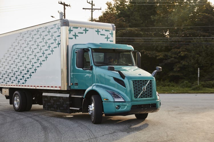 A Volvo VNR Electric truck in motion on a road during daylight, highlighting its design and focus on safety features for battery-powered vehicles.
