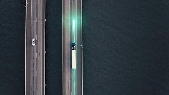 Aerial view of a truck driving on a bridge over water, with a green light trail illustrating a safety or technology feature.