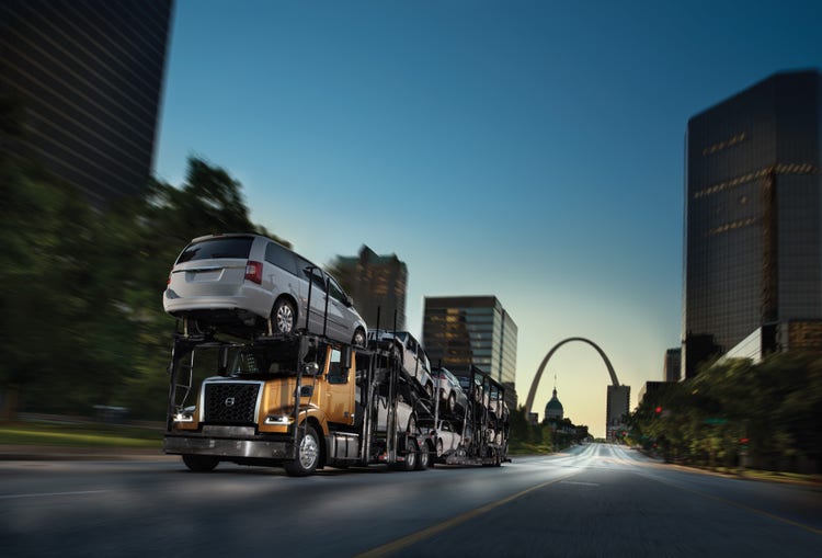 A Volvo VAH truck transporting multiple vehicles on a car hauler trailer, driving on an urban road.