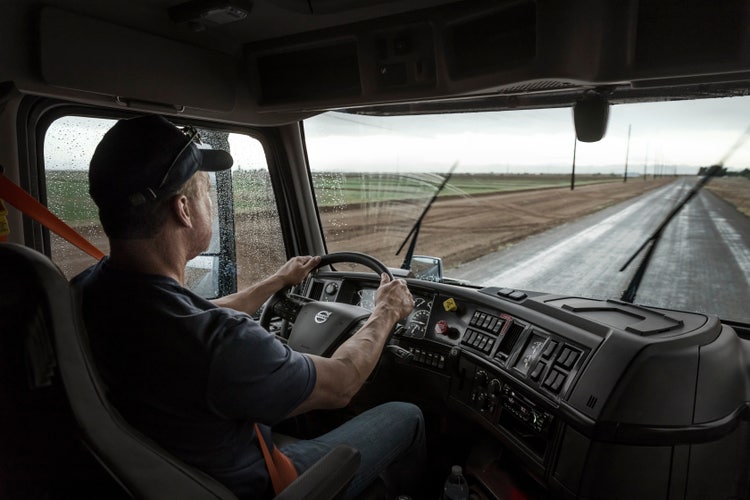A driver operating a Volvo truck in rainy conditions, showcasing the dashboard with integrated camera and radar technology for enhanced safety