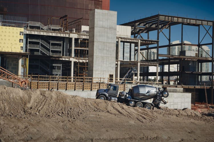 A Volvo VHD cement mixer truck navigating a sloped construction site, with a partially constructed building and urban skyline in the background.