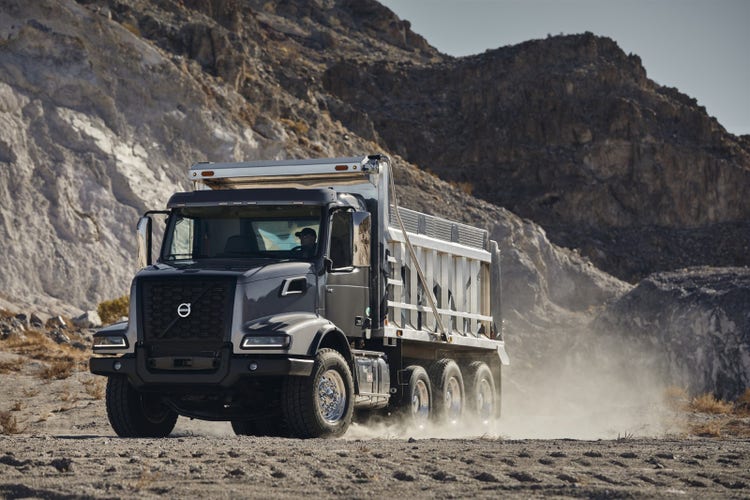 Volvo VHD dump truck driving through a dusty, rocky terrain