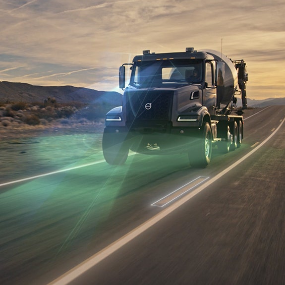 A Volvo VHD truck equipped with a concrete mixer, driving on a highway at sunset, highlighting advanced safety and lane-keeping technology.