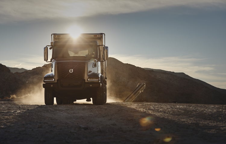 Front view of a Volvo VHD truck on a dusty construction site at sunrise, showcasing its rugged design and capability for demanding job environments.