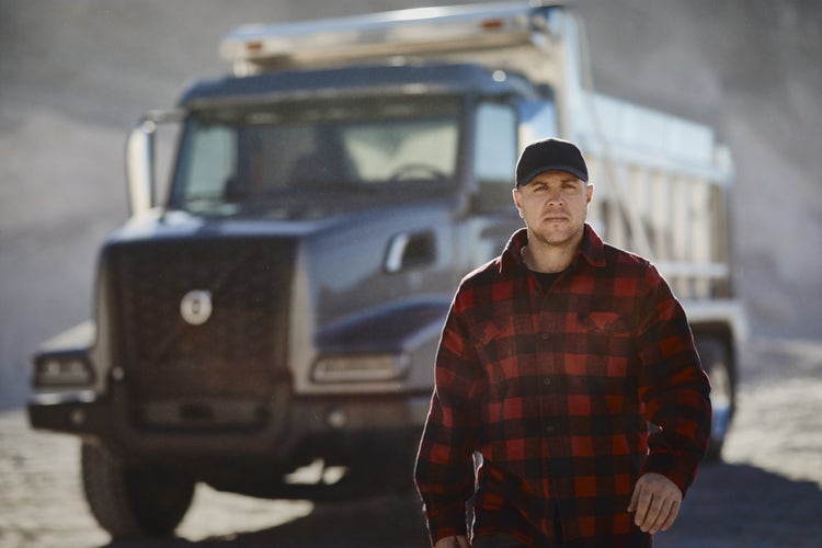 A worker walking at a construction site, with a Volvo VHD dump truck in the background