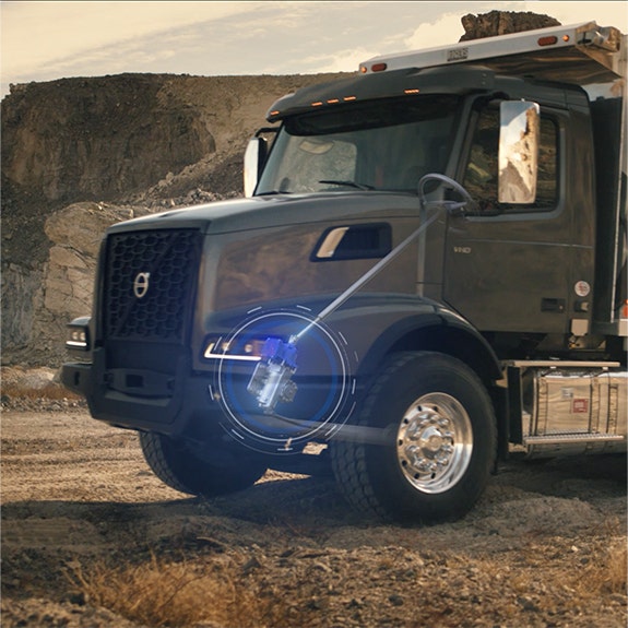 A Volvo VHD dump truck parked at a rugged worksite, with a highlighted detail showcasing its front axle durability and advanced engineering.