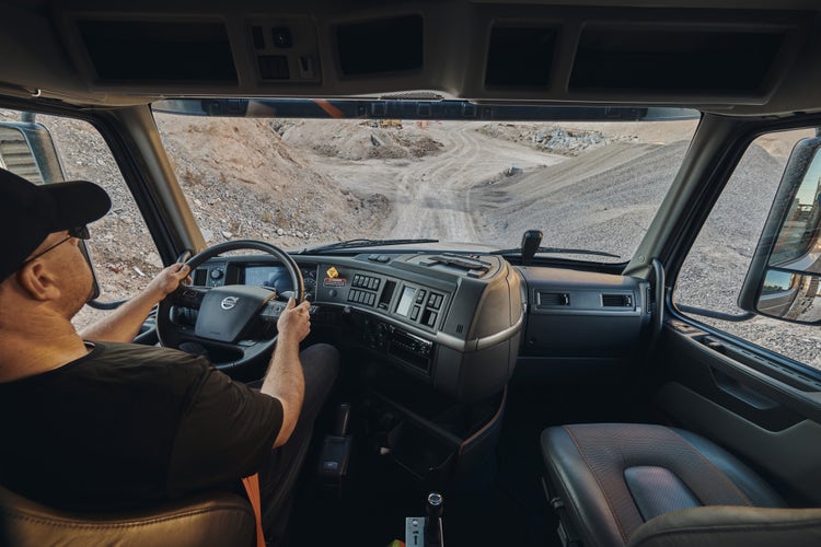 Interior view of a Volvo VHD truck cab with a driver navigating a rugged, unpaved construction site.