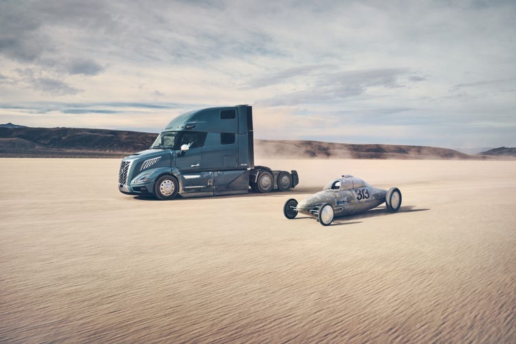 A Volvo VNL truck and a vintage race car driving side-by-side across a desert plain.