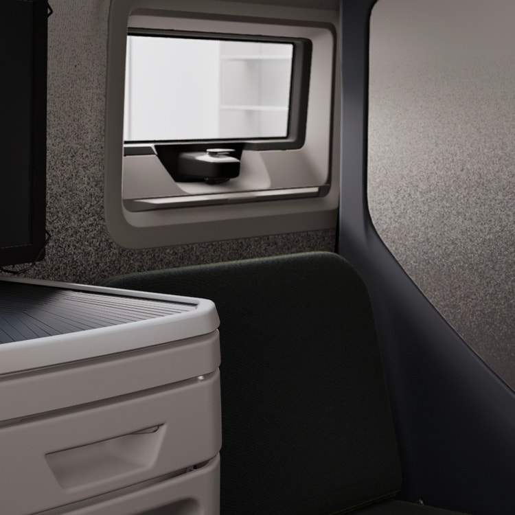 Close-up of a Volvo VNL sleeper cabin with a small window, cushioned seat, and white storage drawer