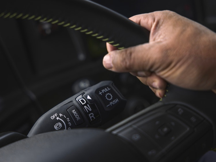 Driver operating the Volvo VNL truck’s steering wheel, highlighting the gear selector labeled "DNR" and integrated control buttons.