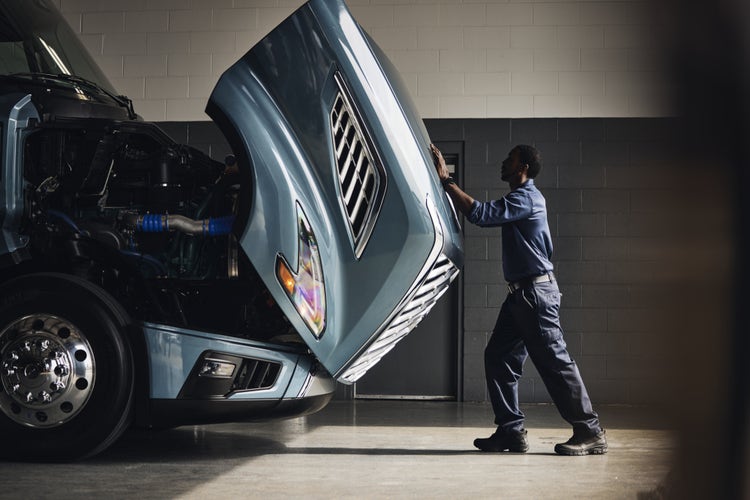 A technician in a workshop opening the hood of a Volvo VNL truck, revealing the engine components.