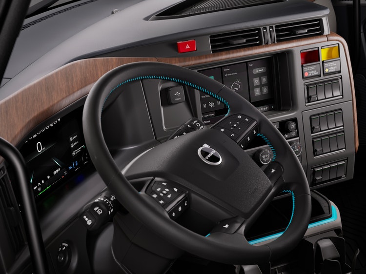 Volvo VNL truck cockpit showing the steering wheel, digital instrument panel, touchscreen controls, and wood-grain trim.