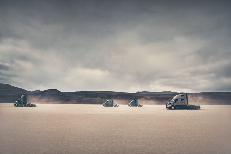 Four Volvo VNL trucks positioned in an open, barren landscape under a cloudy sky.