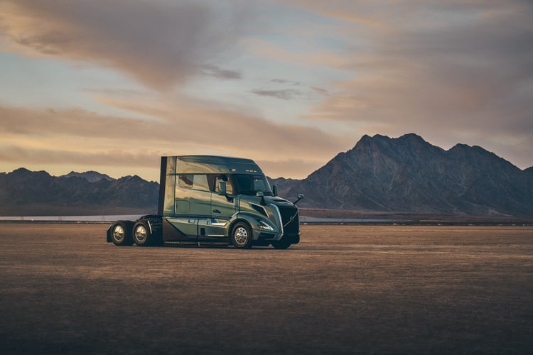 A Volvo VNL truck parked on a flat, open plain with rugged mountains in the background.