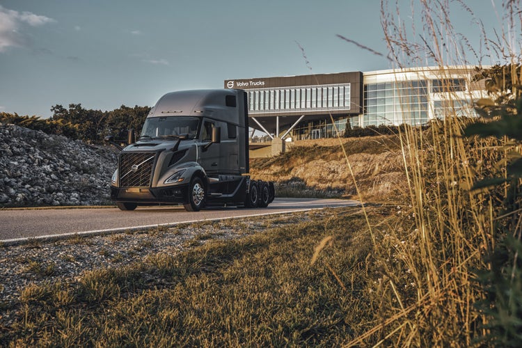 A Volvo VNL truck driving on a road near the Volvo Trucks North America building