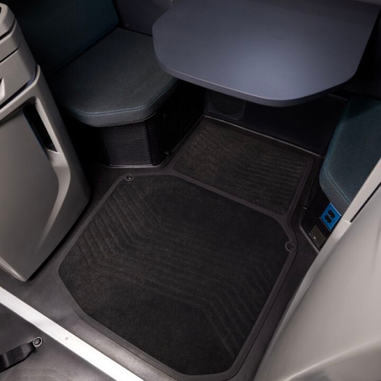 Interior of a Volvo VNL sleeper cab, showing a clean, spacious floor area with dark textured mats, a table, and cushioned seating.