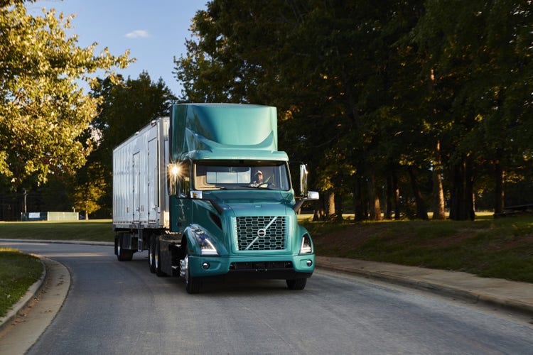 A Volvo VNR Electric truck driving on a suburban road with trees in the background.