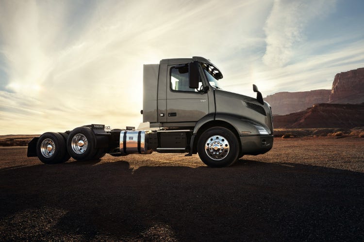 Side profile of a Volvo VNR truck parked in a desert landscape, with sunlight illuminating its sleek design and chrome wheels.
