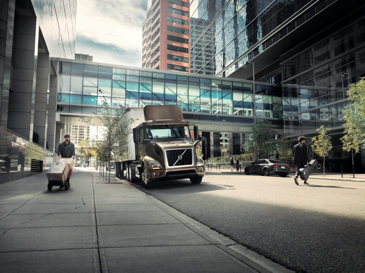 A Volvo VNR truck parked on an urban street near modern glass buildings
