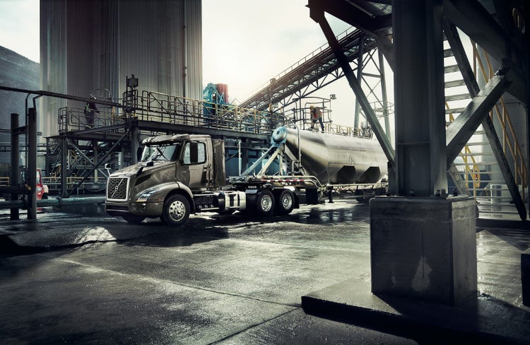 A Volvo VNR truck parked at an industrial facility, hauling a polished tanker trailer