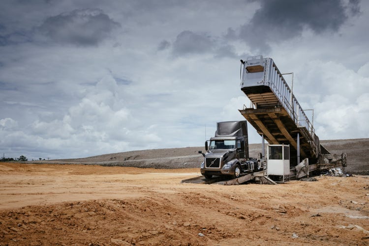 A Volvo VNR truck positioned beneath an industrial conveyor system in a barren, sandy area.