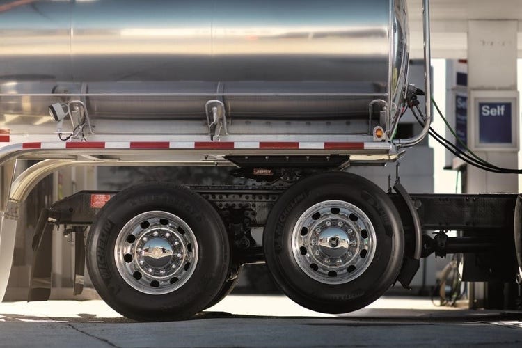 Close-up of a polished tanker trailer and rear wheels of a Volvo VNR truck at a fueling station.