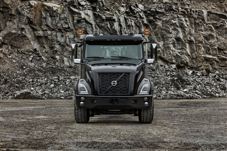 Front view of a black Volvo VNX truck parked at a rocky quarry, highlighting its robust grille, LED headlights