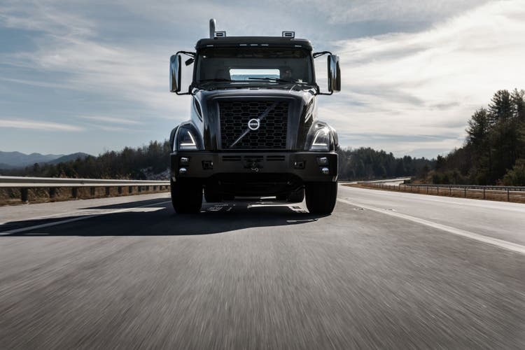Front view of a black Volvo VNX truck driving on a highway, emphasizing its powerful grille design and robust performance for heavy-duty transport.
