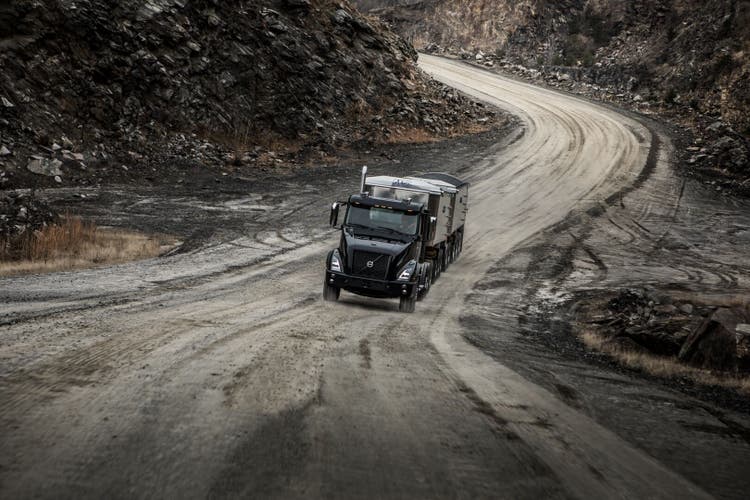 A black Volvo VNX truck hauling a heavy trailer on a winding dirt road in a quarry, showcasing its strength and reliability in demanding terrains.