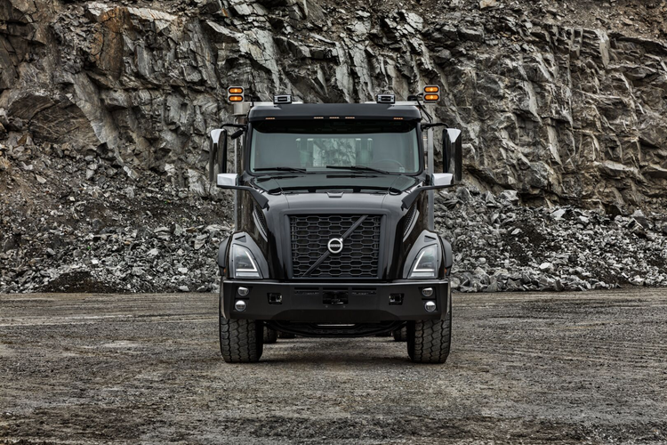 Front view of a black Volvo VNX truck parked at a rocky quarry, highlighting its robust grille, LED headlights