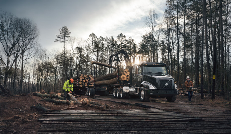 A black Volvo VNX truck at a logging site, loaded with large timber logs
