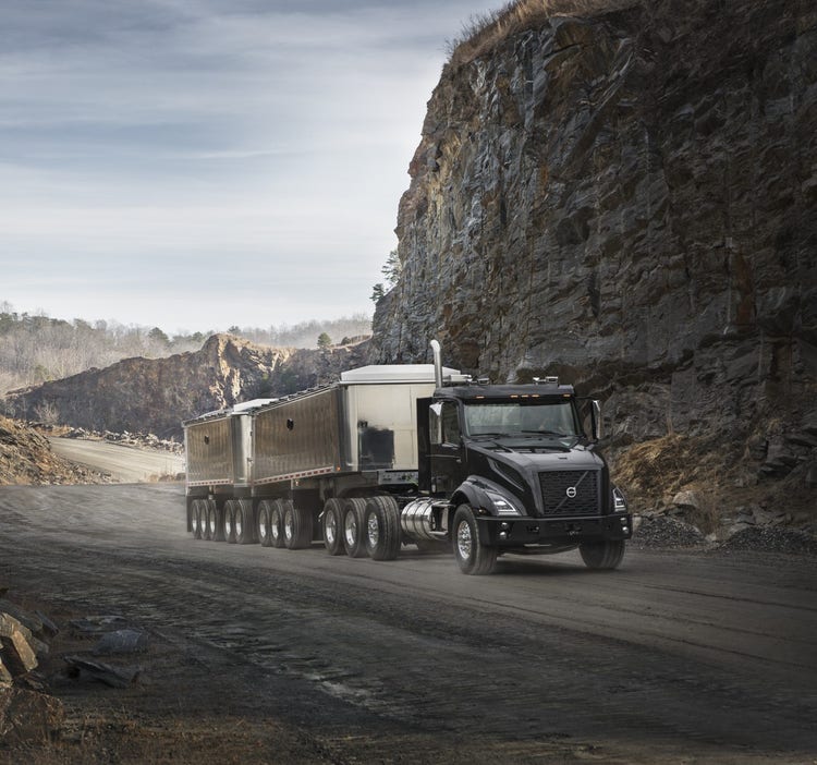 A black Volvo VNX truck hauling heavy trailers through a rocky quarry, demonstrating its strength and capability in demanding work environments.