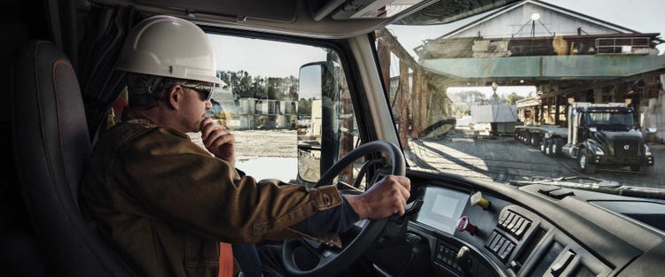 A driver sits inside a Volvo VNX truck cab, viewing a worksite through the windshield, highlighting the truck’s ergonomic interior and jobsite readiness.